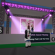 A Roblox character wearing a hat stands in front of a pink stage.